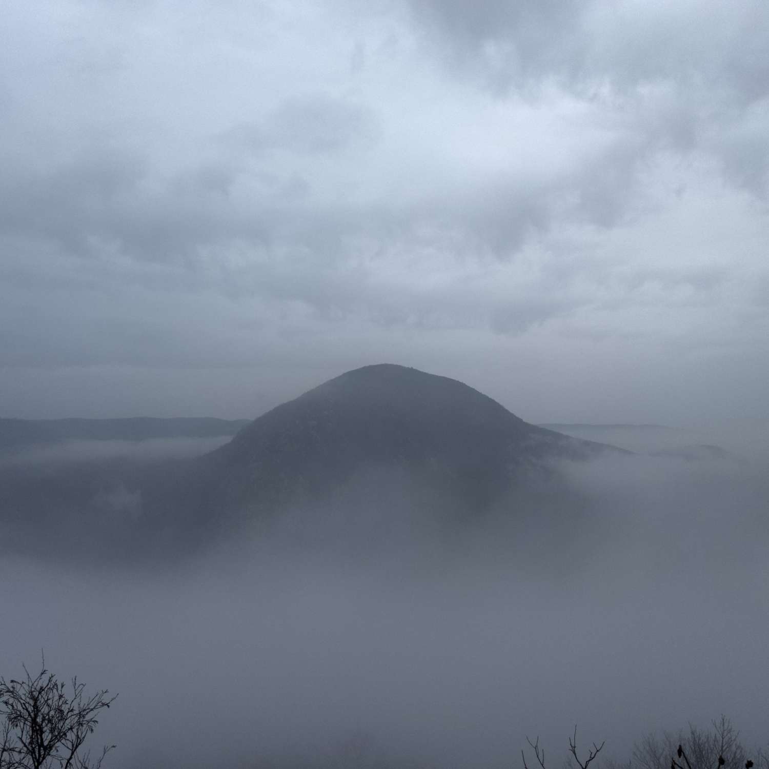 a photo of a mountain, wrapped in dense, humid fog, under a cold sky